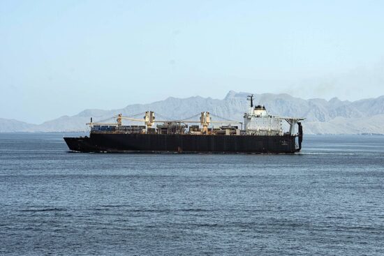 USNS PFC Dewayne T. Williams sailing through the Strait of Hormuz with mountains behind it.